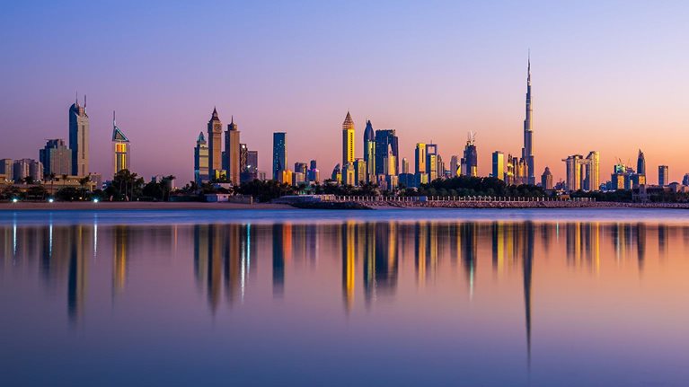 Beautiful sunset showing the Dubai Skyline with mirrorlike reflections in the lake - stock photo