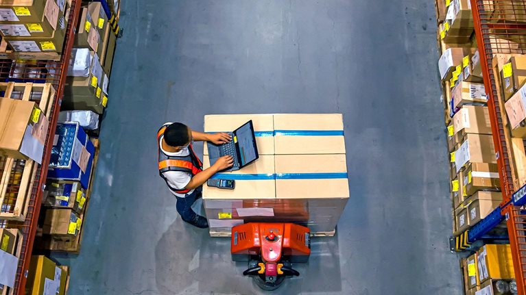 Top view of warehouse worker using laptop to check location of goods