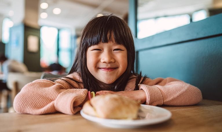 Lovely cheerful girl smiling joyfully at the camera while enjoying meal in a cafe.