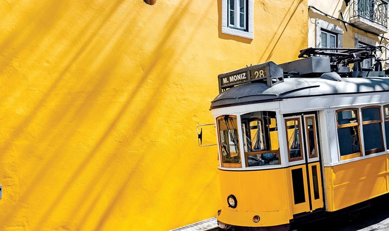 Yellow tram moving past yellow building in Lisbon, Portugal