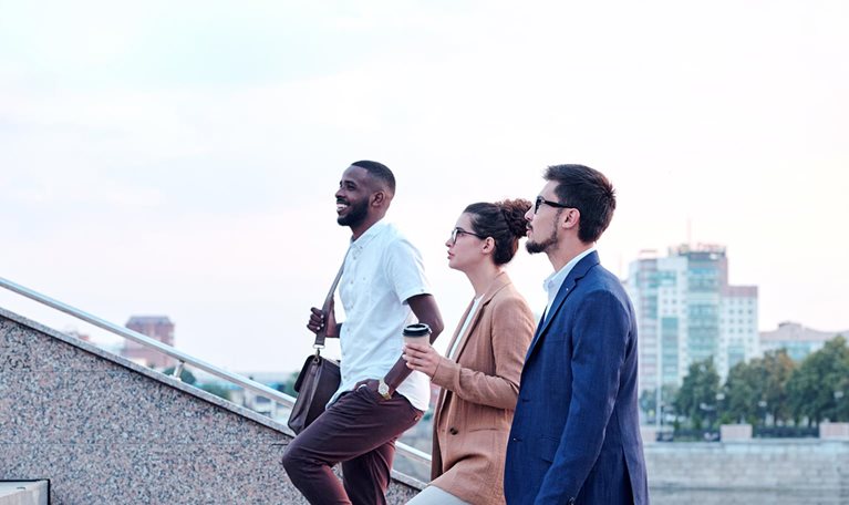 Side view of a confident multi-ethnic group of young professionals chatting while walking up a flight of stairs