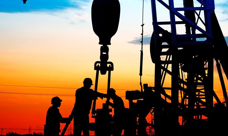 Silhouetted workers operating an oil drilling rig, against a vivid sunset sky with gradients of orange, red, and blue.