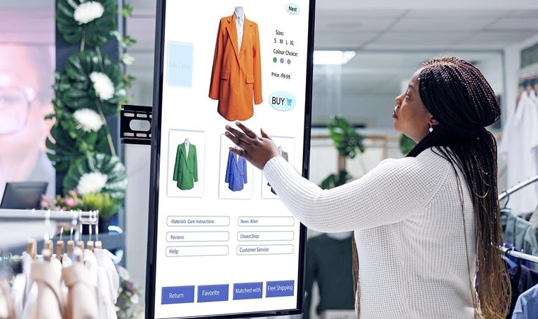 Image of a woman selecting clothes using an interactive touch screen monitor in a clothing store.