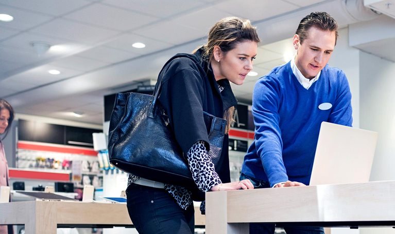 Salesman assisting female customer in buying laptop at store