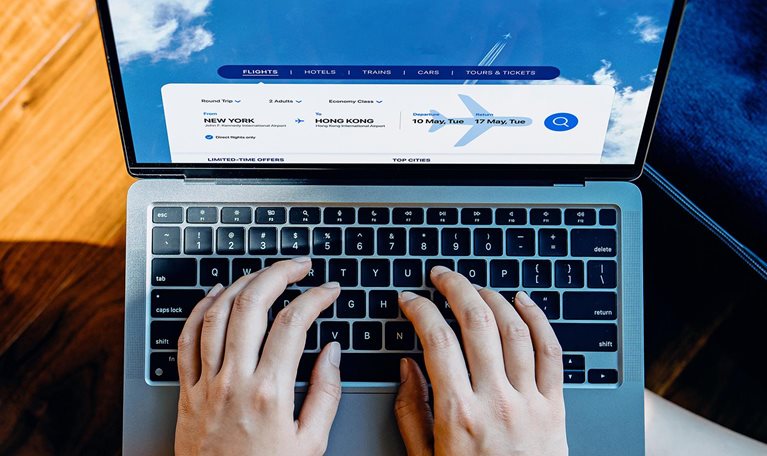 High angle shot of young woman booking flight tickets on airline website with her laptop, a packed suitcase by her side.