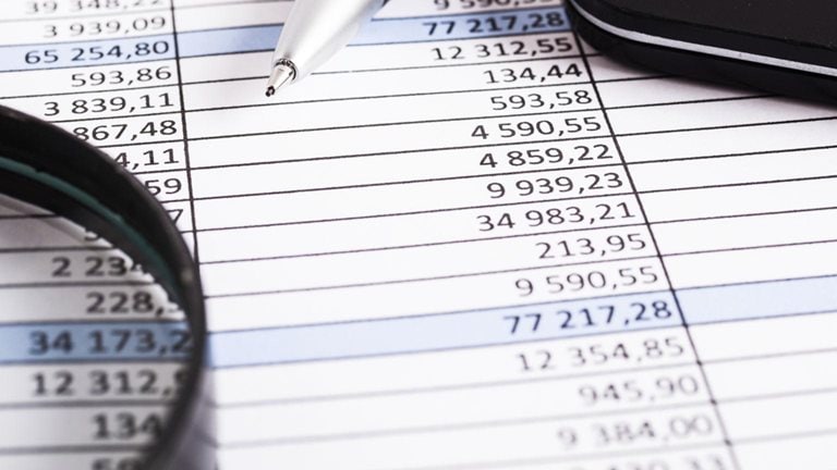 Stock image of a printed spreadsheet with pen and magnifying glass
