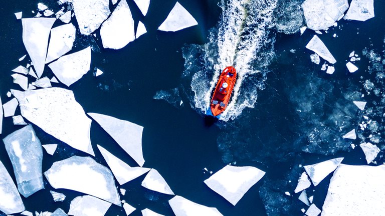 Wintery aerial view of a red ice-breaker ship pushing through cracked sea ice