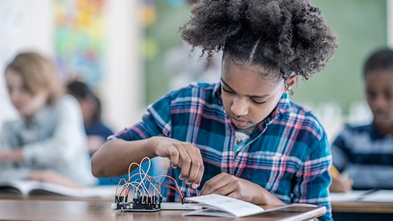 A child wearing a plaid shirt, working on a circuit board.