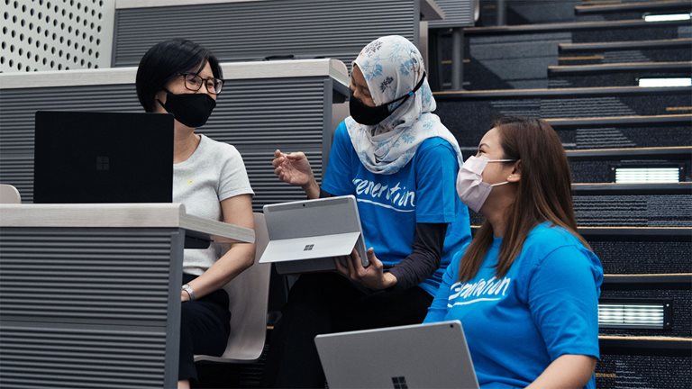 Three women talking while working on laptops