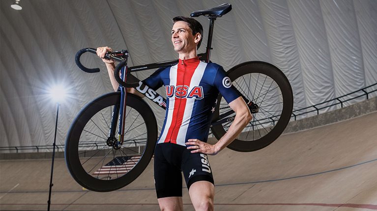 Derek Bouchard-Hall poses in his racing uniform with his bike on the Olympic racing track