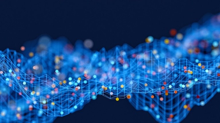 An abstract rendering of a data wave, with interconnected blue lines forming a grid-like structure. Spheres in shades of red, yellow, and blue, representing data points within raw data sets, are distributed across this grid, set against a solid dark blue background.
