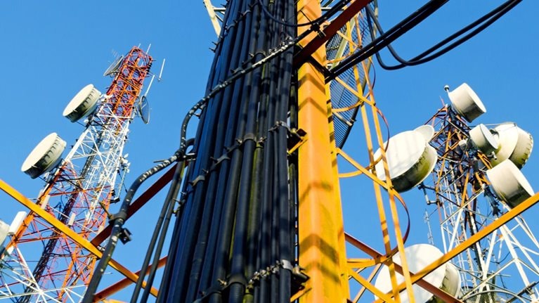 A low-angle view of a complex of telecommunication towers against a clear blue sky.