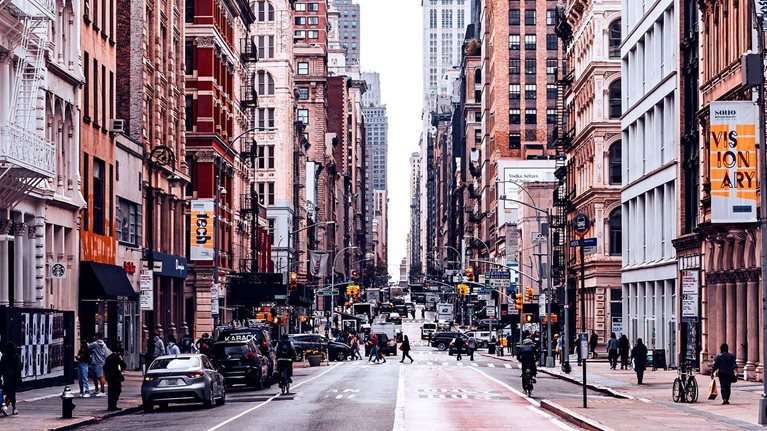 A bustling New York City street lined with historic buildings, shops, and pedestrians.