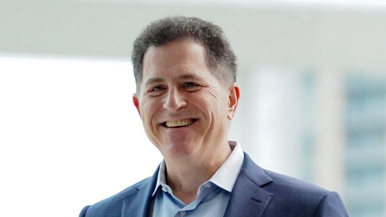 Michael Dell, wearing a blue suit jacket and smiling in an office filled with natural sunlight.