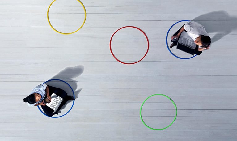 Business women with laptops sitting across the room from each other in 2 of 5 multi-colored circles