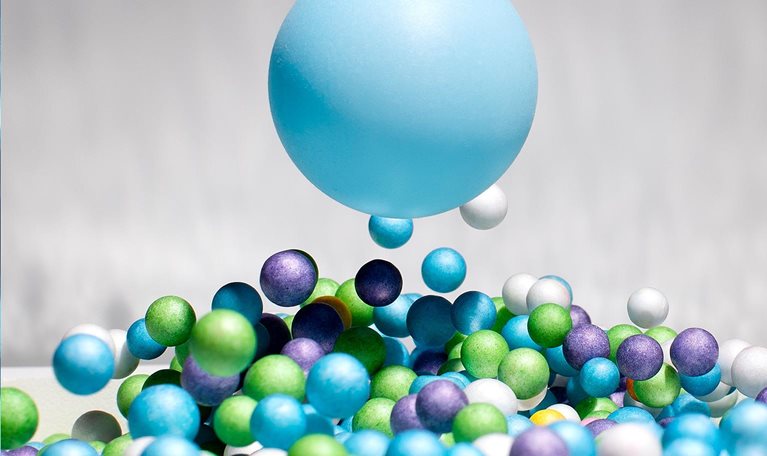 One large blue ball in mid air above many smaller blue, green, purple and white balls