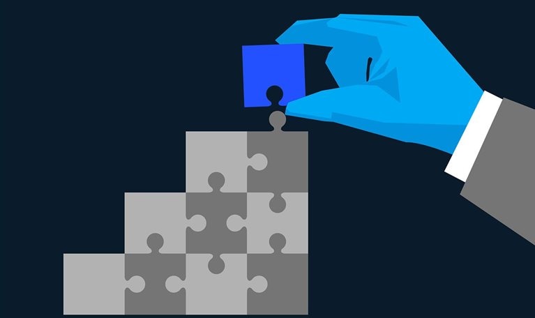 A hand is placing the final blue puzzle piece into a larger structure made of grey pieces. The image is an illustration symbolizing problem-solving, integration, or building a solution.