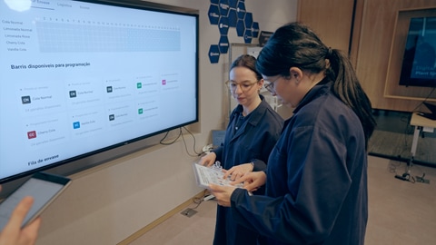 Two workers looking at a chart and standing next to a large monitor
