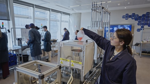 Lab worker pouring a red liquid into a large container