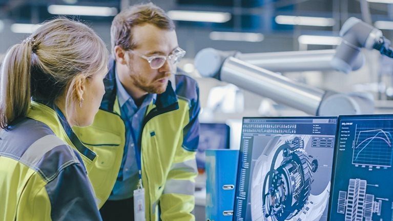 At the Factory: Male Mechanical Engineer Holds Component while Female Chief Engineer Work on Personal Computer, They Discuss Details of the 3D Engine Model Design.