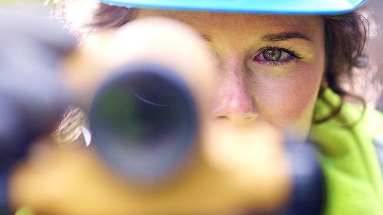 Close up of young female surveyor looking through the lens of a theodolite checking levels on a site.