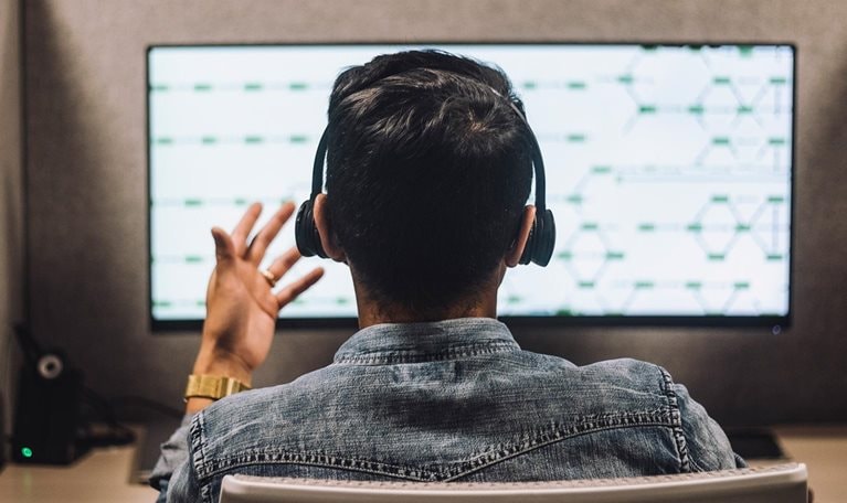 Rear view of young male customer service executive talking through headset sitting at desk in illuminated call center