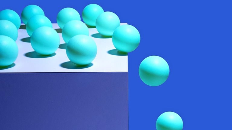 Multiple balls on top of a box with a few of them rolling and falling off the edge.