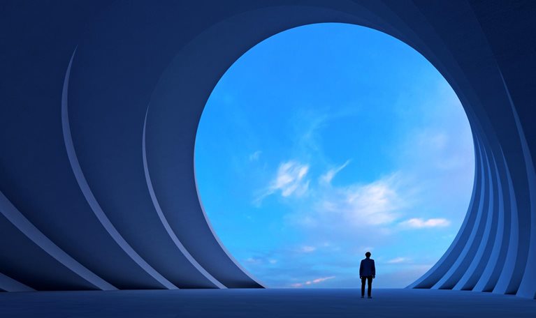 A person stands in a vast blue architectural space, looking through a large circular opening toward a bright sky.