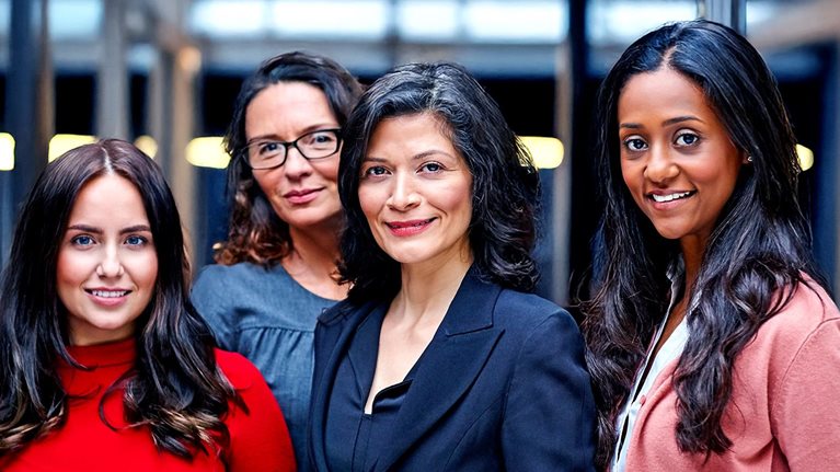 A diverse group of four professional women look confidently forward.