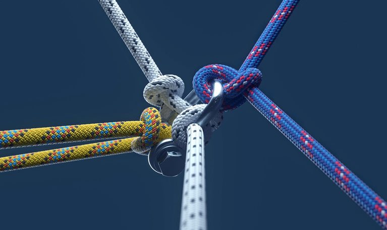 Close-up image of three colored ropes knotting together on dark blue background.