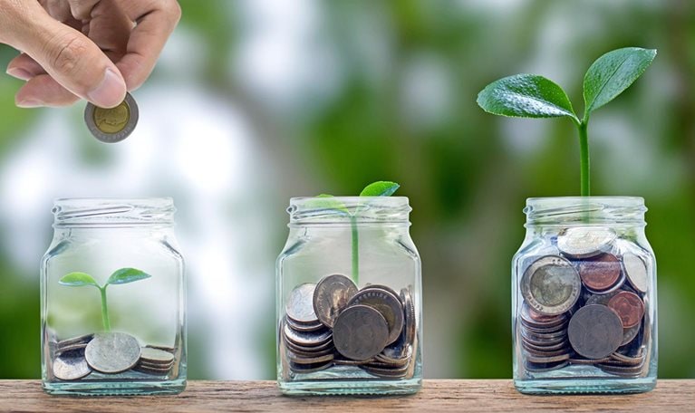 A hand putting a coin into a glass bottle containing coins