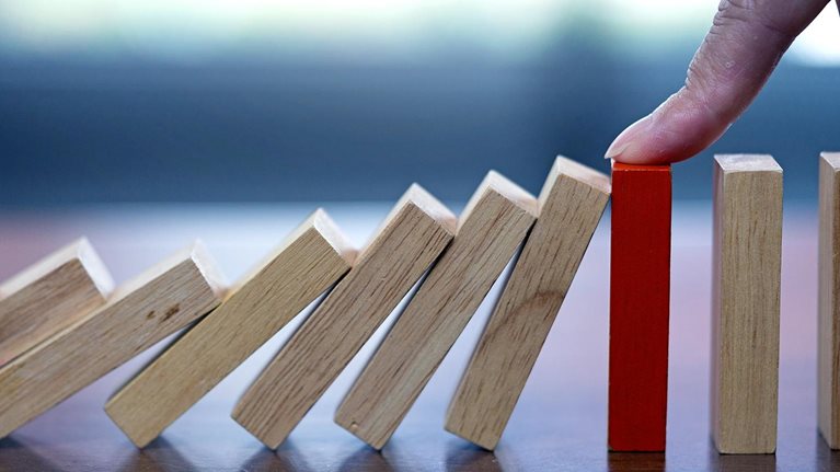 Close up image of a finger reaching down and stopping falling dominos.