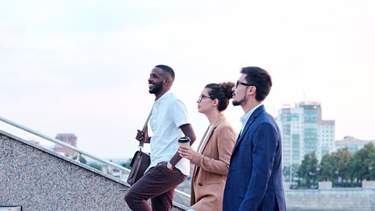 Side view of a confident multi-ethnic group of young professionals chatting while walking up a flight of stairs