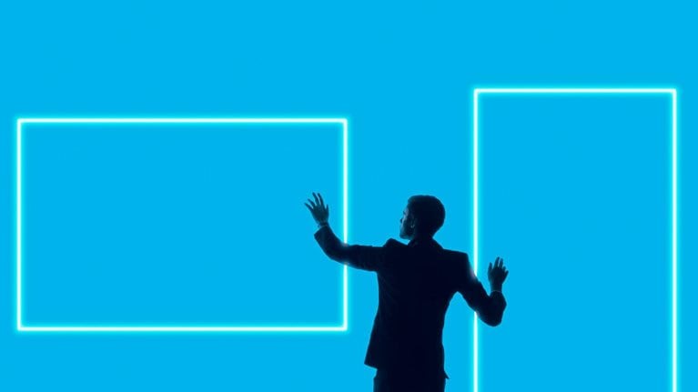 A silhouetted man in a suit stands against a bright blue background, reaching toward two glowing rectangular outlines that resemble digital screens or frames.