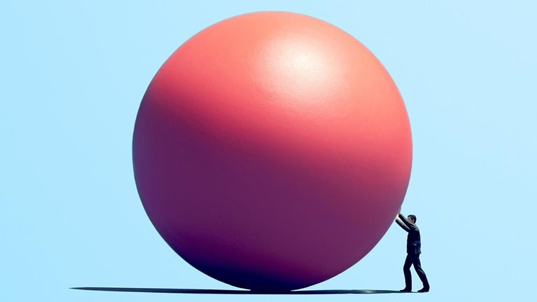 Person pushing a large pink sphere across a flat surface against a light blue background.