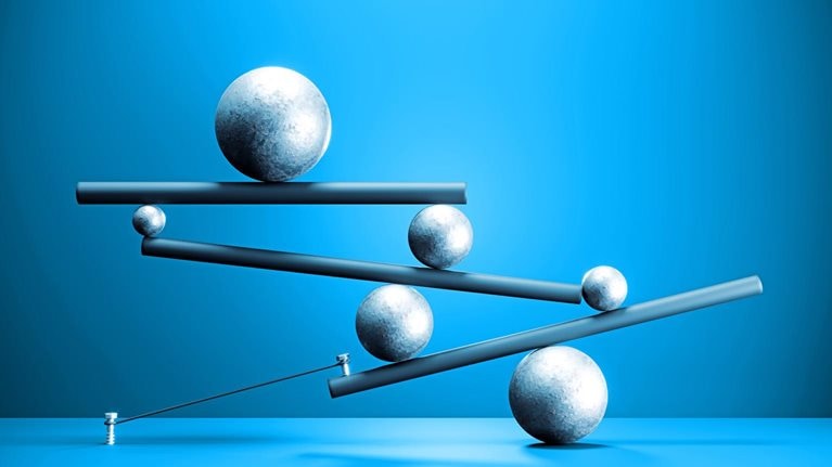 Several spheres of different sizes are balanced across tilted beams, forming a delicate, interconnected structure. The composition against a blue background suggests tension and the careful balancing of forces.