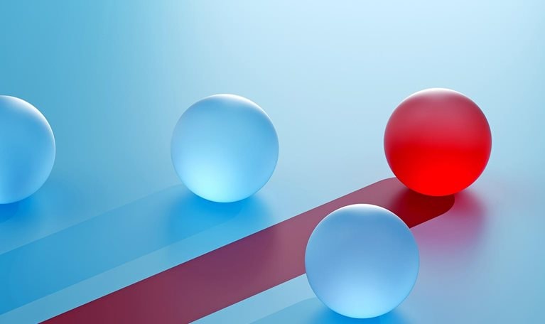 A single red sphere breaks away from identical blue spheres, moving on a distinct path. It symbolizes competitive advantage—standing out through differentiation, focus, and strategic direction.