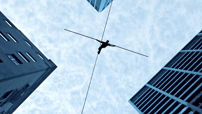 Performer walking a tightrope in between four high rise buildings.