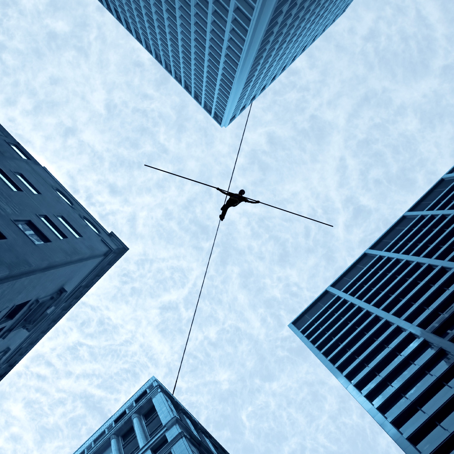 Performer walking a tightrope in between four high rise buildings.