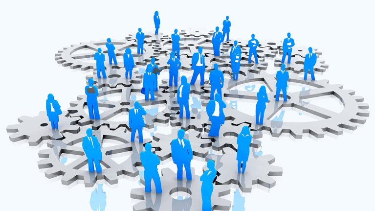 An isometric illustration features a group of individuals dressed in business attire standing on interlocking gears. The people are depicted in blue, while the gears are silver.