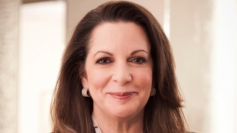 A professional headshot of Julia Stewart. She has long dark brown hair and is wearing a dark blazer over a patterned blouse while smiling gently.