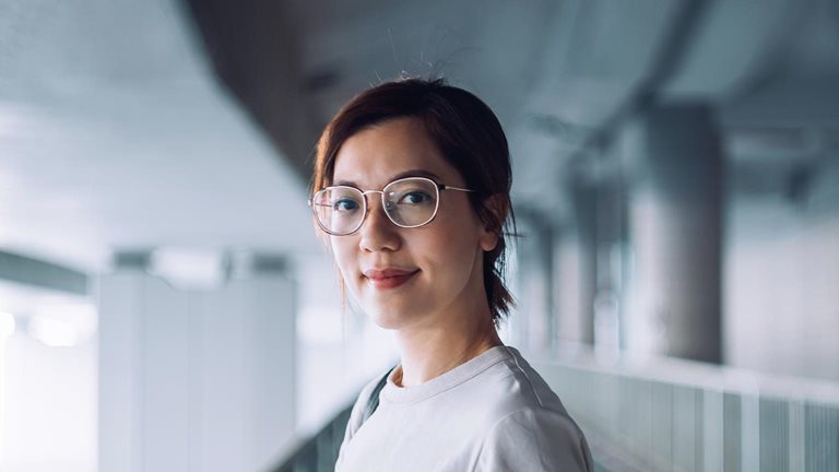 Portrait of confident and successful young Asian businesswoman looking at camera with smile, standing against urban bridge in the city - stock photo