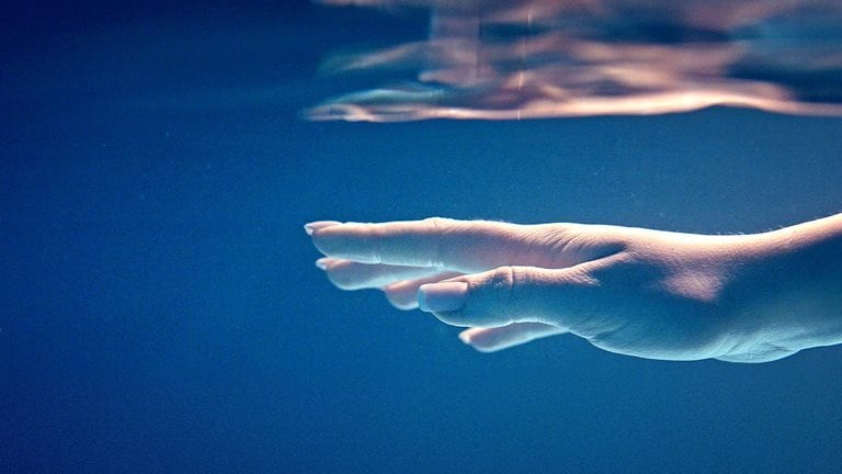 Image of a hand underwater with light dancing over it, reflecting on the surface above.