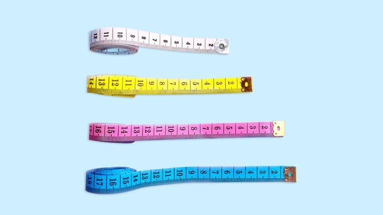 Four measuring tapes are positioned vertically on a light blue backdrop. Each tape is stretched out to varying lengths and placed in increasing order from the longest to the shortest.