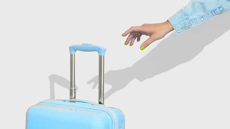 A hand with bright yellow nails reaches for the handle of a blue suitcase.