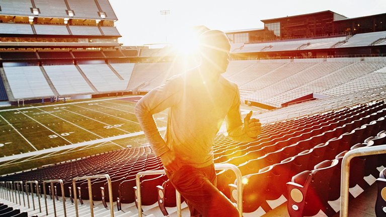 Male athlete running stairs during workout in empty stadium at sunset