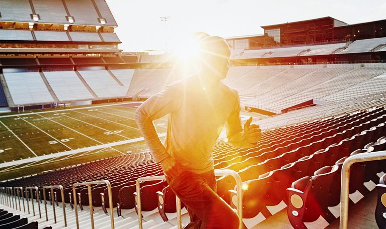 Male athlete running stairs during workout in empty stadium at sunset