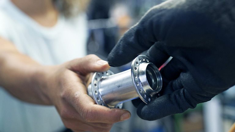 A close up of a technician handing her colleague a bike part while working together in a bicycle workshop