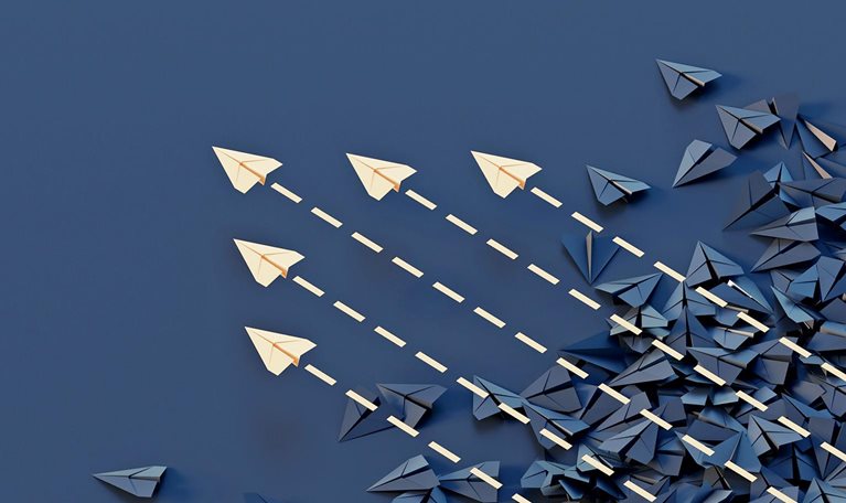 Conceptual image showing a jumble of dark paper planes with an organized group of colored planes flying through and above them.