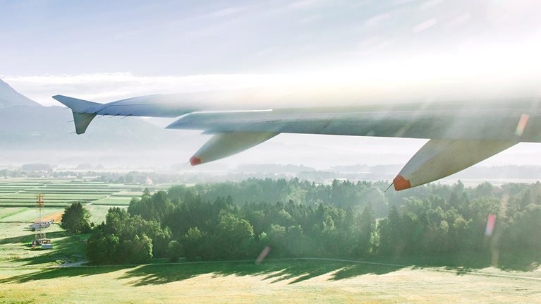 View of lush green fields outside plane window as wing flies forward.